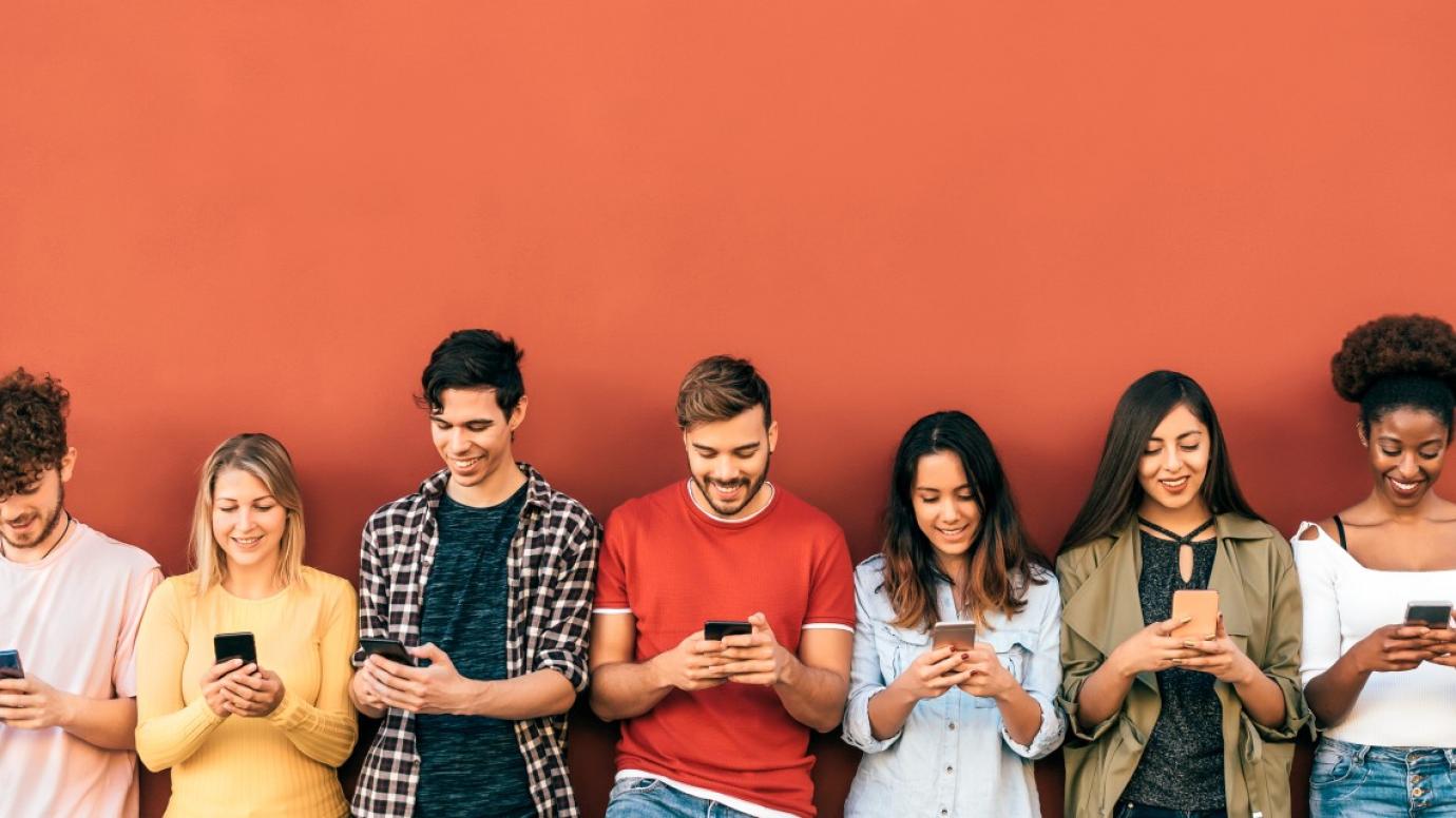 Group of teenagers in a line by a red wall playing with smartphones