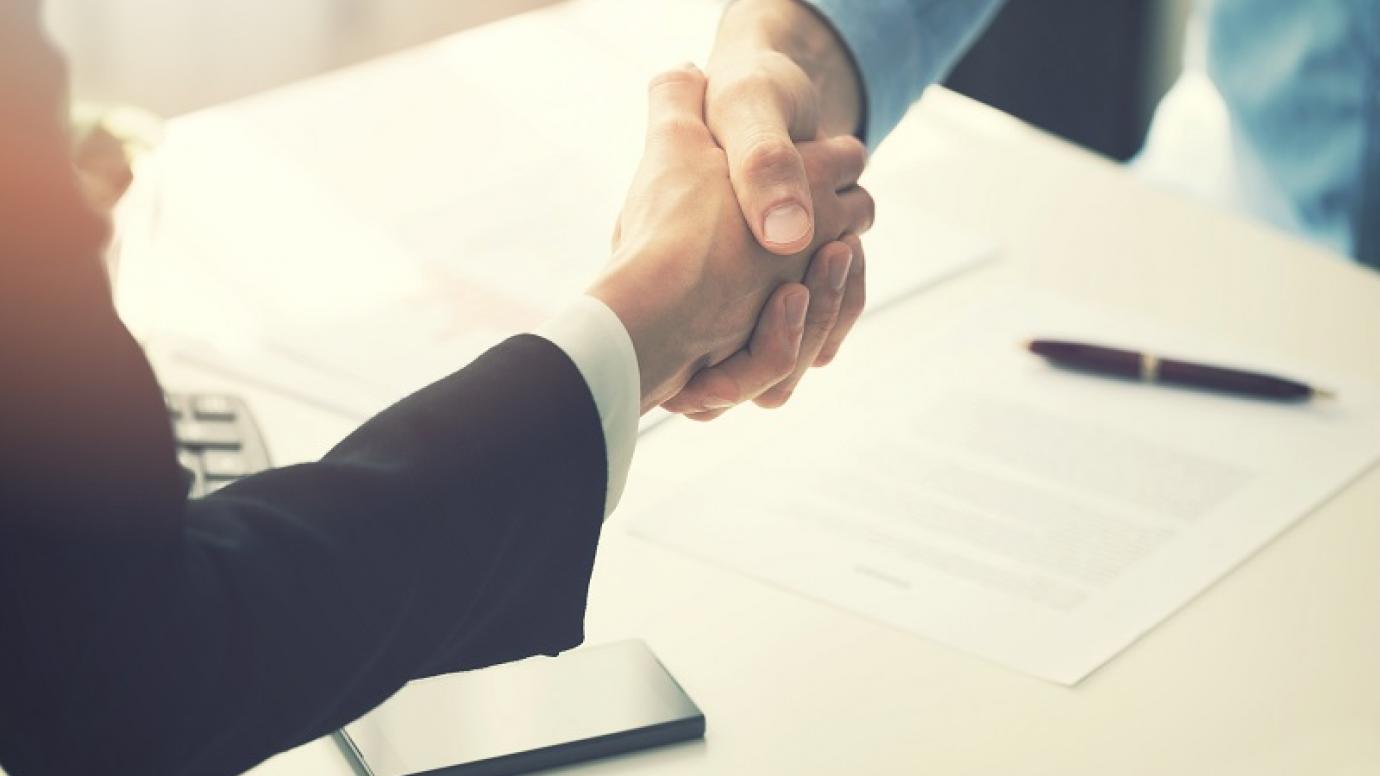 Two people shaking hands over a signed document