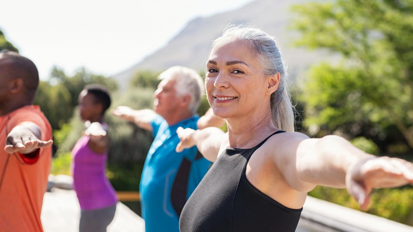 Portrait of happy senior woman practicing yoga outdoor with fitness class.