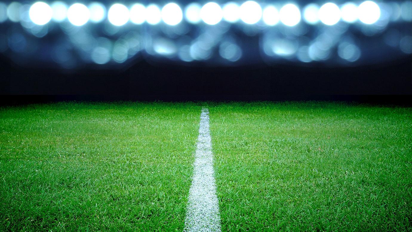 Close up on a football pitch at night with lights in the background