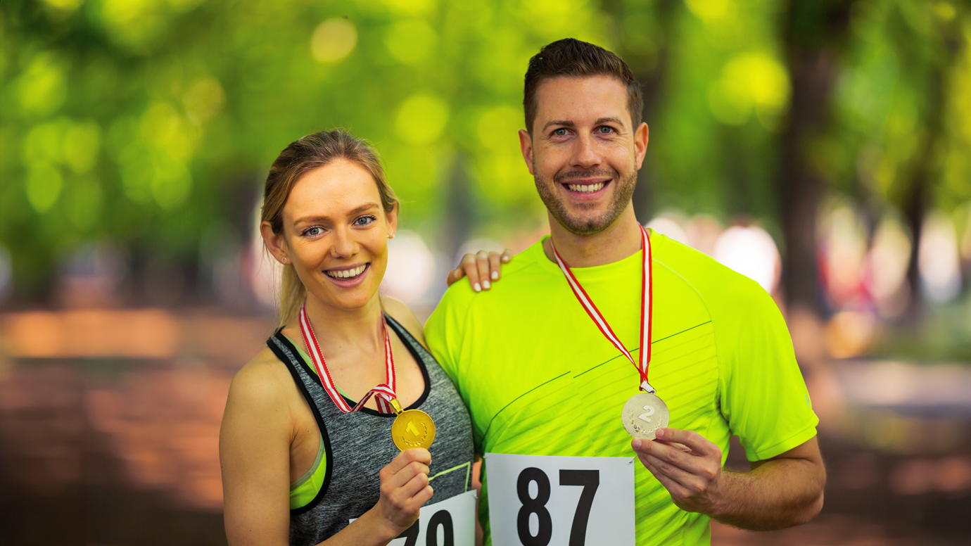 2 athletes, woman and man after the race, holding medals received in their hands